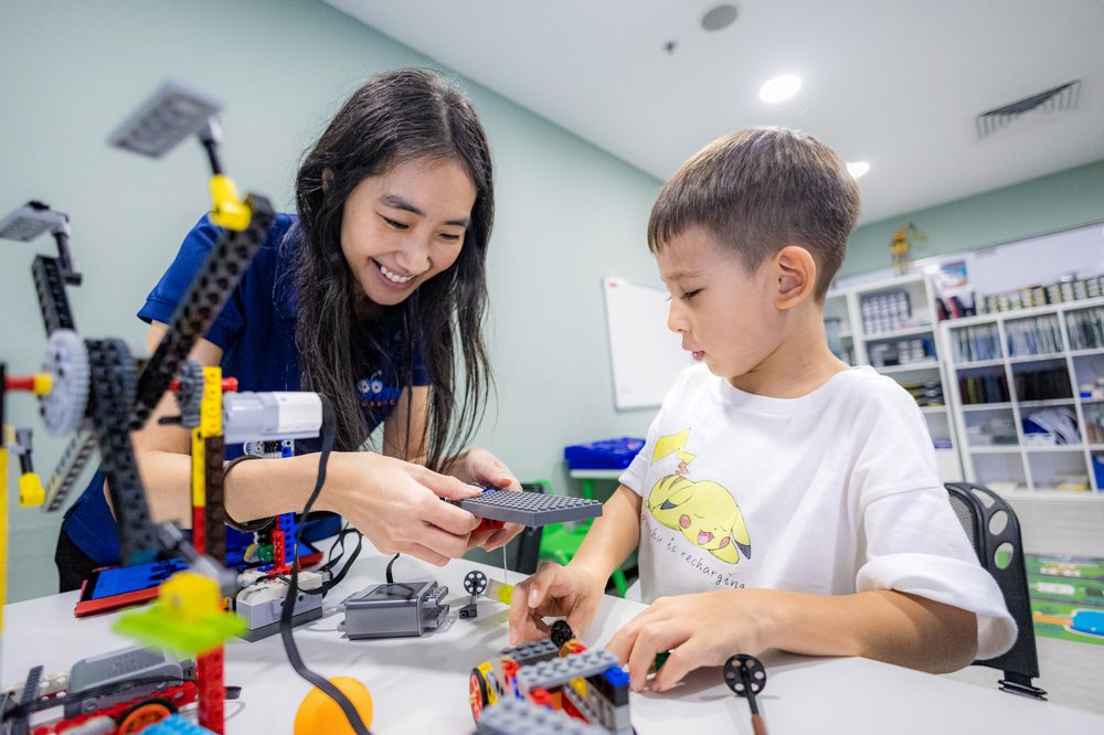 An instructor guiding a young student building a LEGO robot
