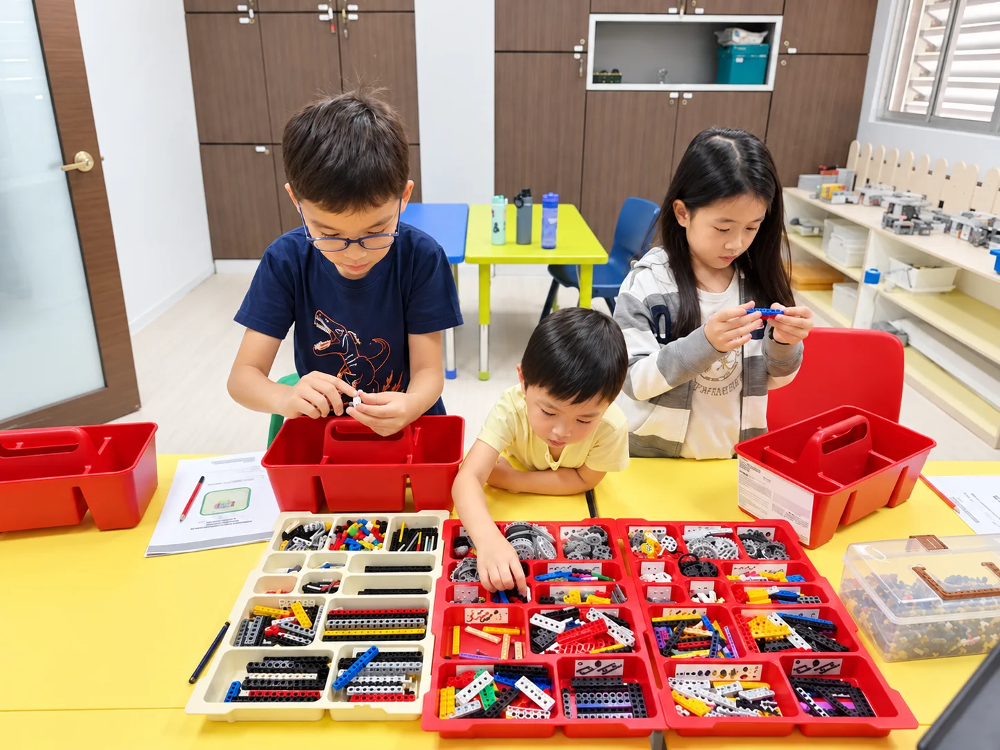 Three students assembling models with robotics parts at a classroom table